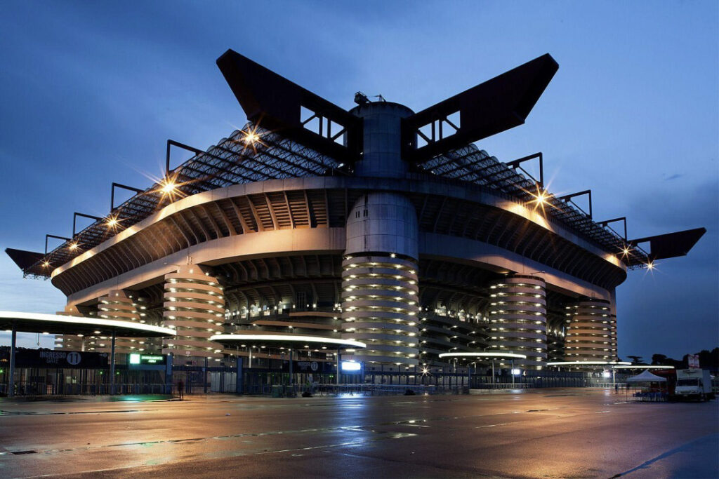 Stadio di calcio illuminato al tramonto, con le aree di accesso e parcheggio